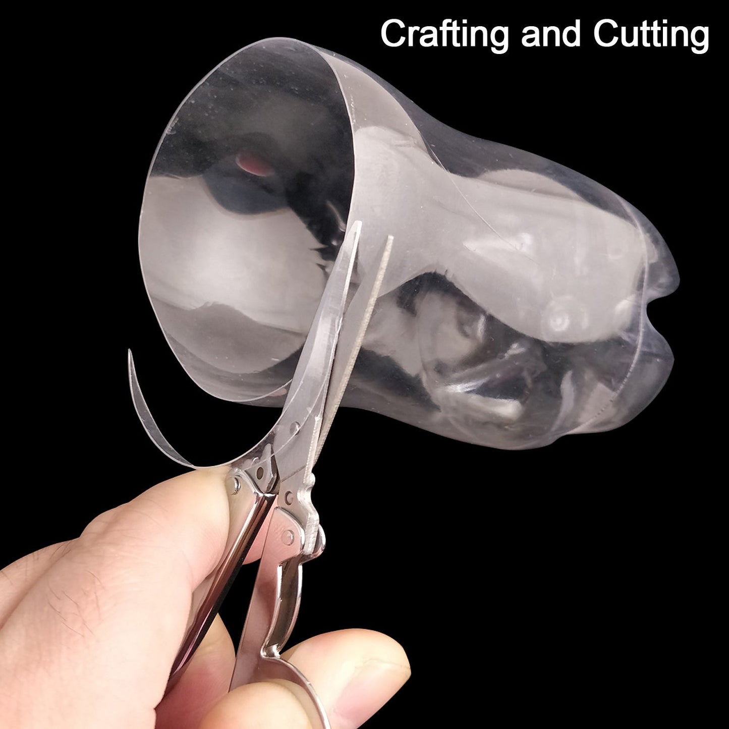 A hand uses open silver folding scissors to cut a clear plastic bottle against a black background.