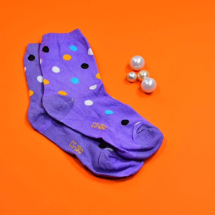A pair of purple crew socks with multi-colored polka dots and white pearls on a vibrant orange background.