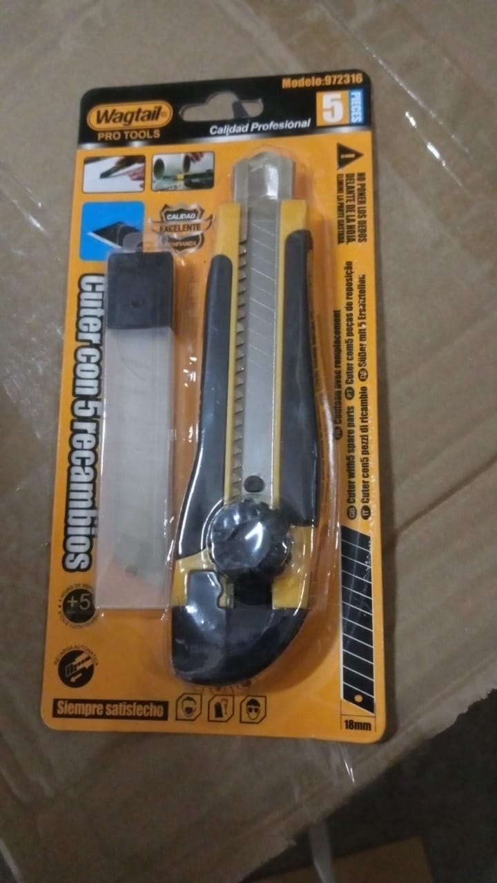 The utility knife and replacement blades are shown in their retail packaging on a brown cardboard surface.
