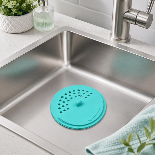 A teal round silicone drain cover with small holes sits in a stainless steel kitchen sink.