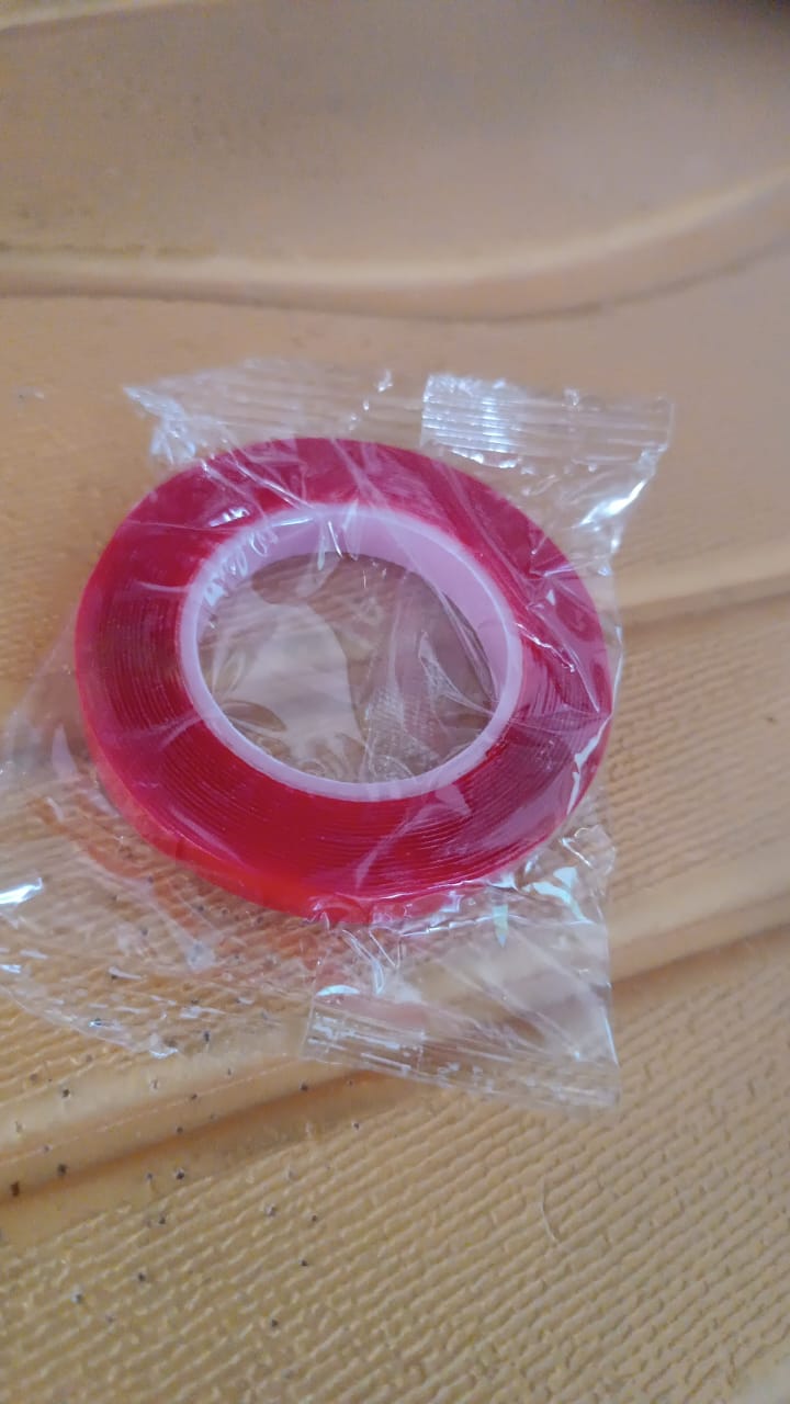 A roll of red-lined clear tape is visible through its clear plastic packaging on a textured brown surface.