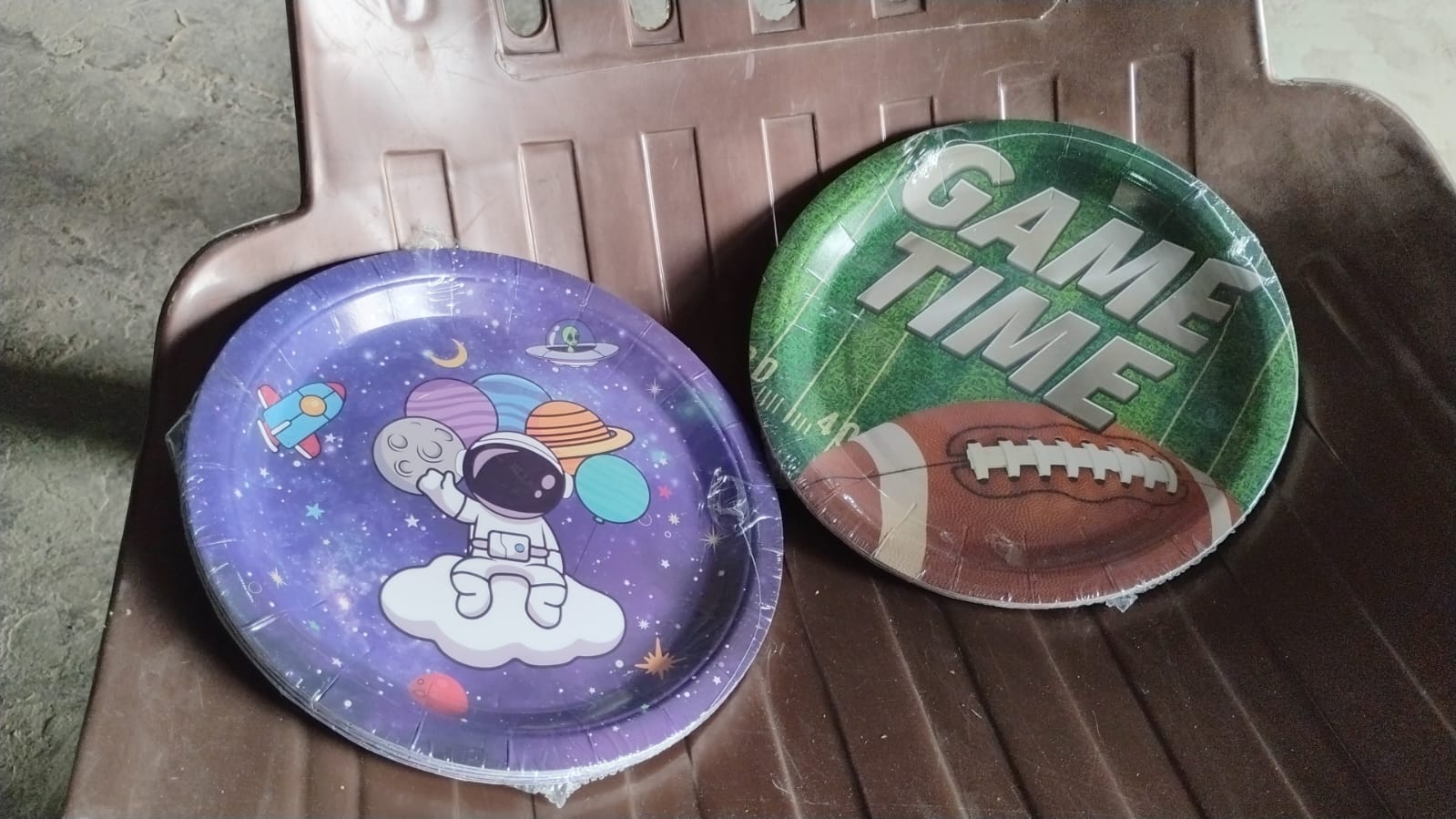 Neatly stacked disposable paper plates with festive football and space designs.