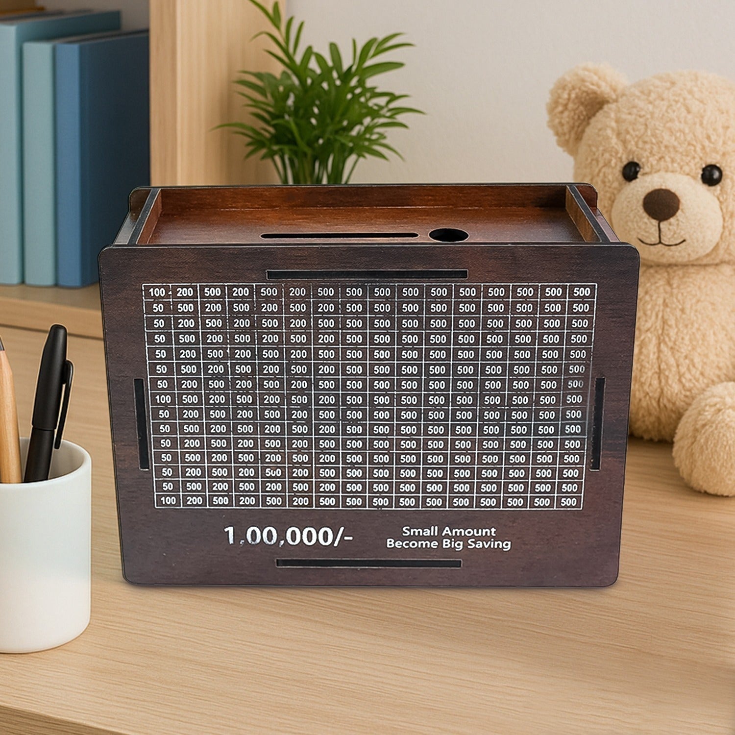 A dark brown wooden savings box with a white grid tracker on a wooden desk, with a teddy bear and pens in the background.