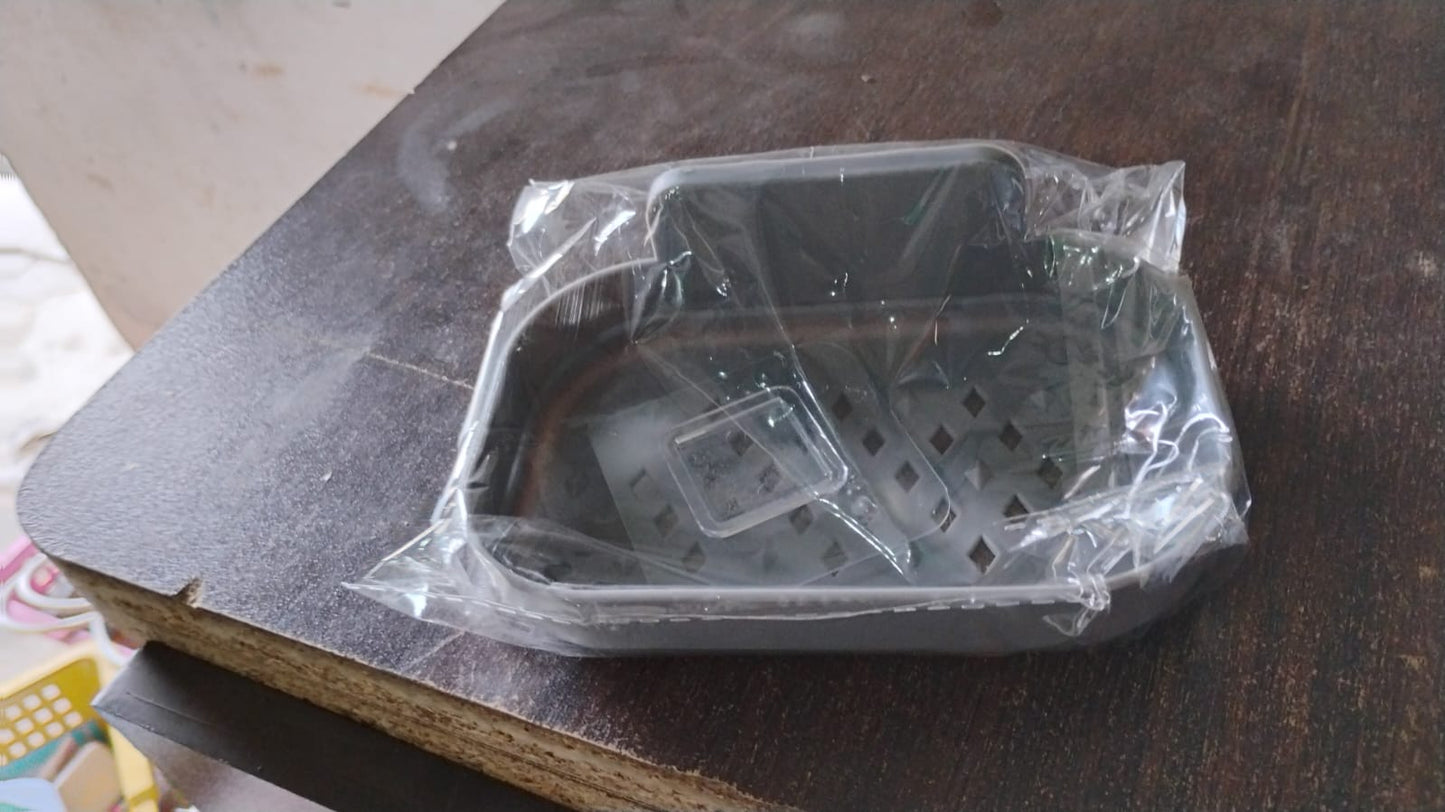 A gray self-adhesive soap dish is packaged in clear plastic on a dark brown wooden surface.