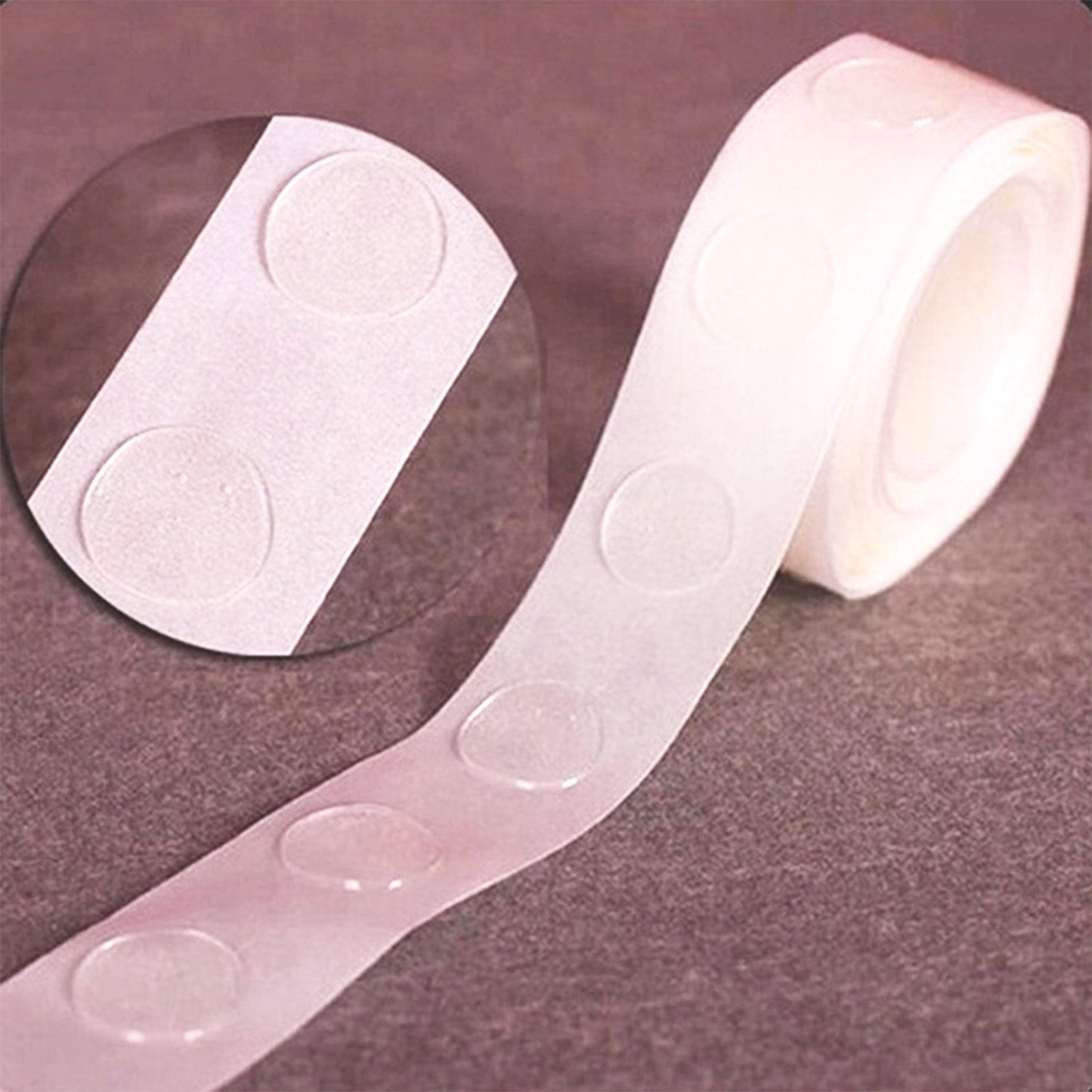 A close-up of a roll of clear, round glue dots on a white paper backing, with a magnified view in a circular inset.