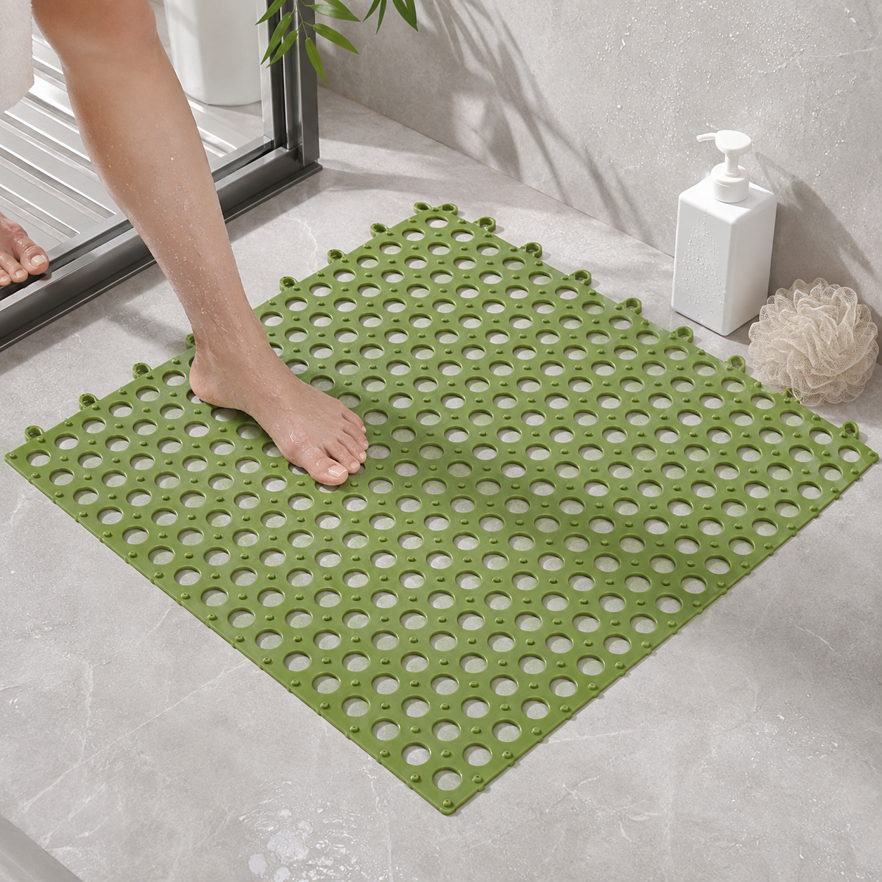 A foot steps onto a green anti-slip mat with circular holes on a tiled bathroom floor next to a shower.