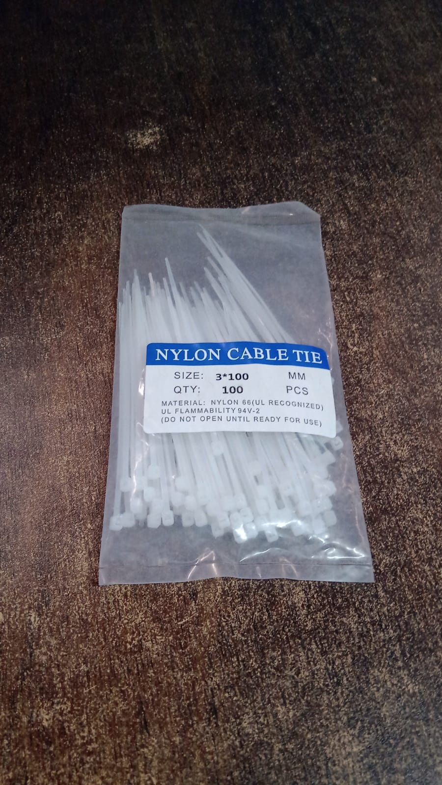 A clear plastic bag of white nylon cable ties with a blue label, resting on a textured brown surface.
