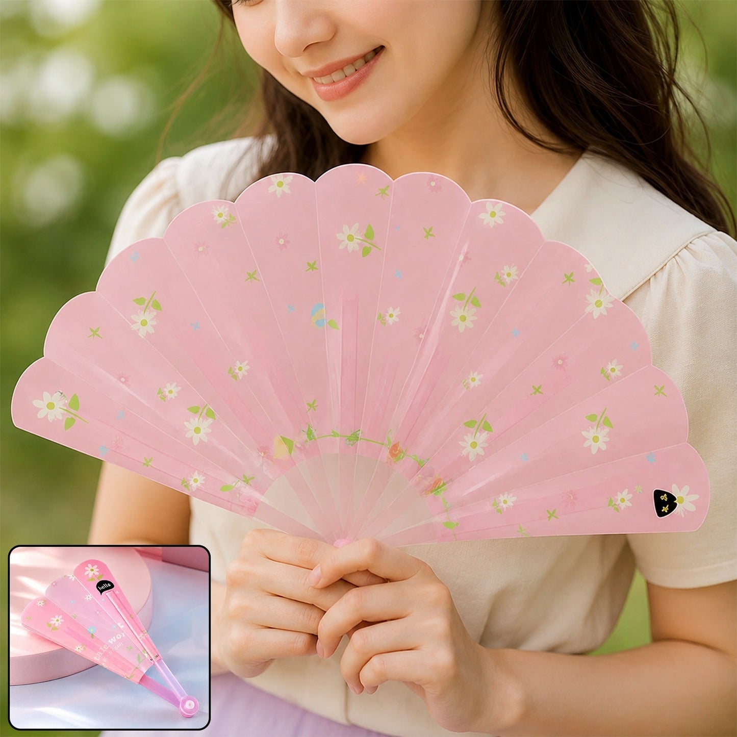 A smiling woman holds an open pink fan with white floral patterns, a smaller folded fan in the bottom left corner.
