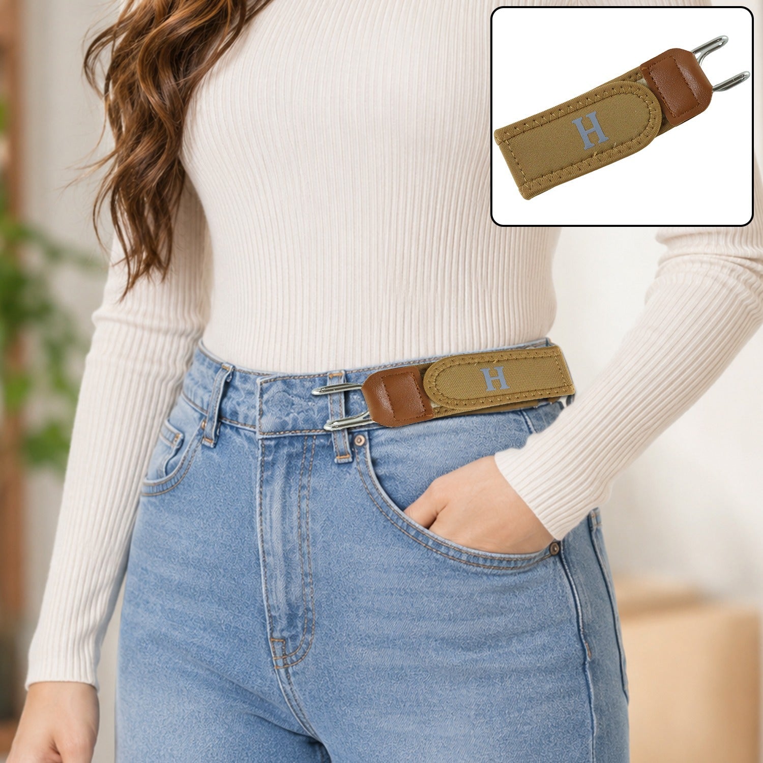 A woman wears light blue jeans and a white top with a camel-colored elastic belt featuring a gray 'H' and silver hooks.