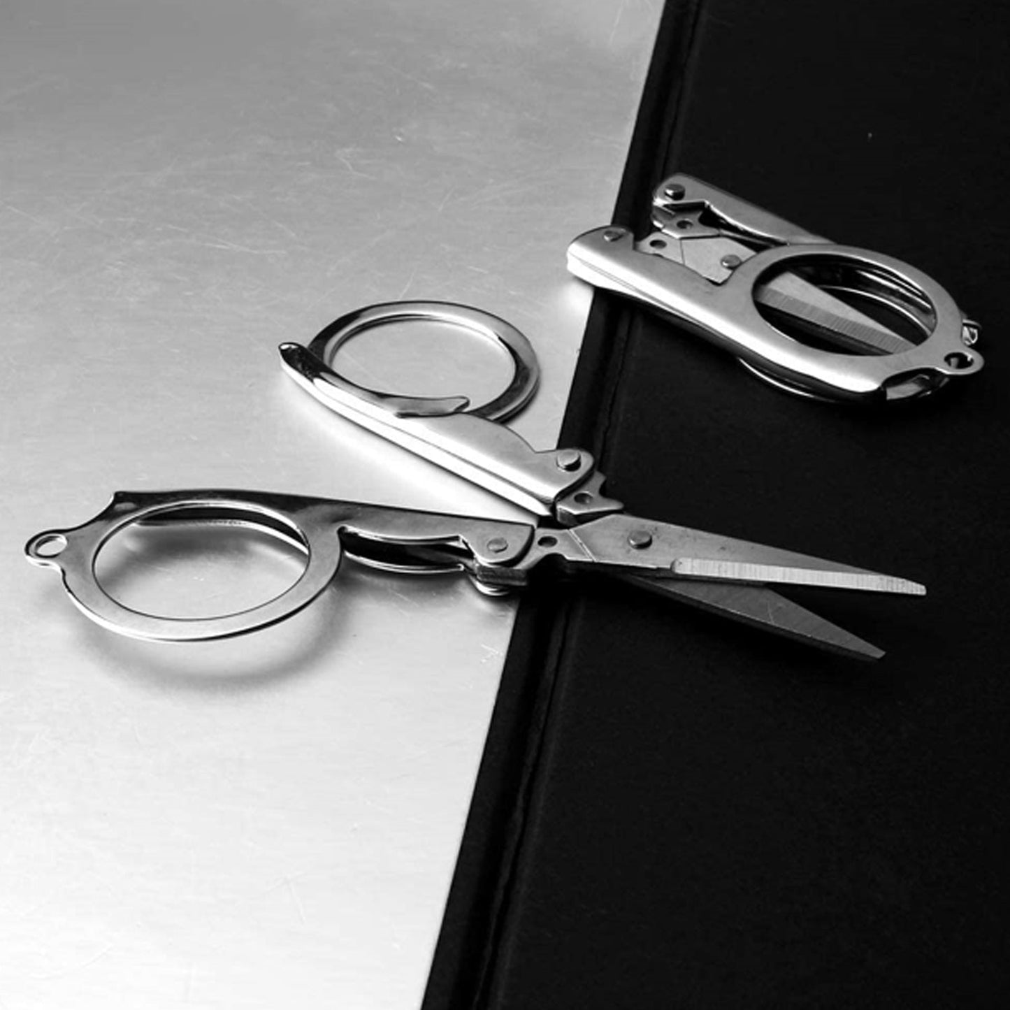 Two silver folding scissors, one open and one closed, rest on a black and silver surface.