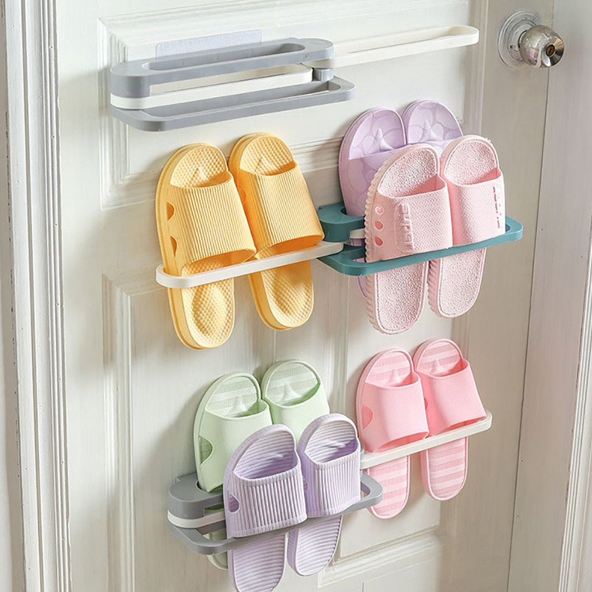 Three folding shoe racks in gray and teal hold various colored slippers on a white door.