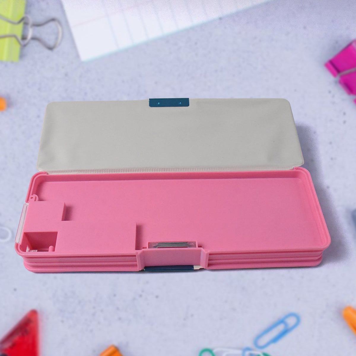 Open pink pencil case showing its empty compartments and a gray lid, surrounded by office supplies.