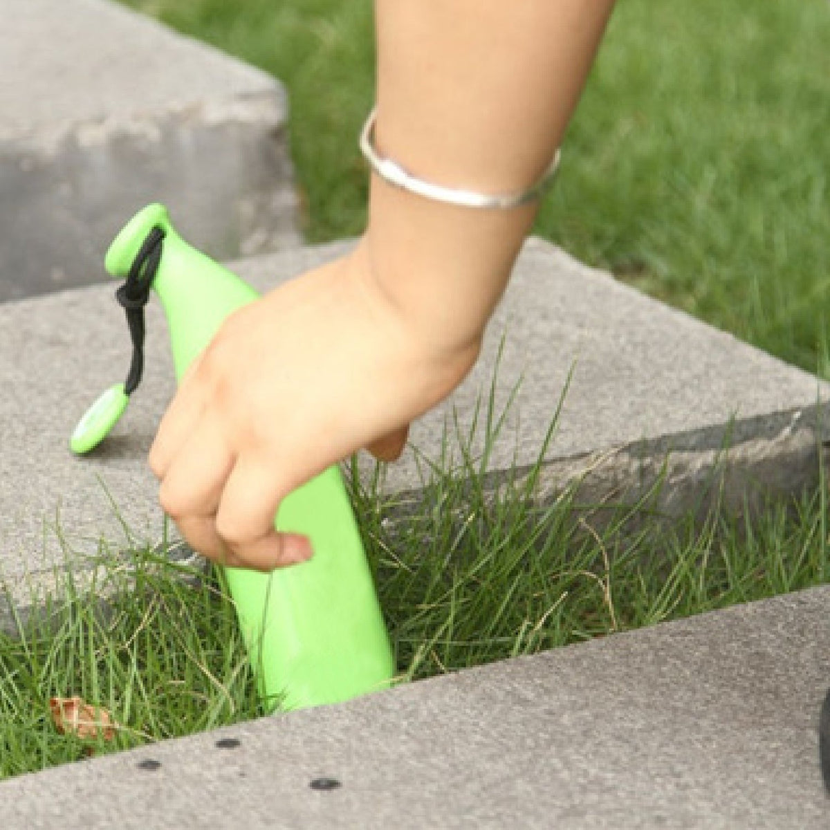 A hand places a green banana-shaped umbrella case into a grassy area between concrete steps.
