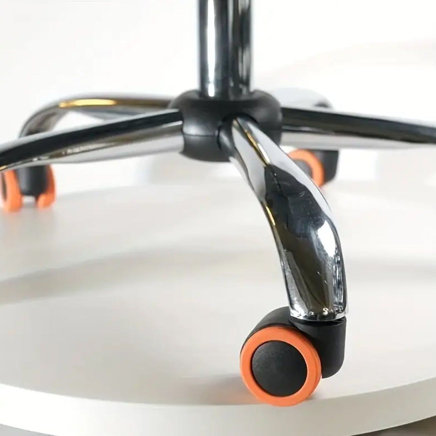 Close-up of an office chair's chrome base with black wheels and orange silicone covers on a white surface.