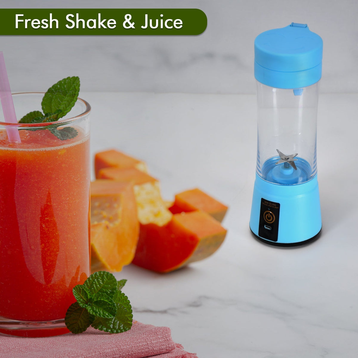 A blue portable juicer blender stands next to a glass of orange juice and sliced papaya on a white marble surface.