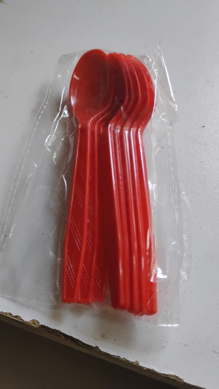 A stack of red plastic spoons with textured handles sealed inside clear plastic packaging.