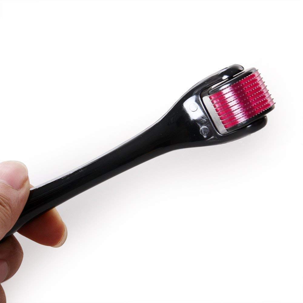 A hand holds a black derma roller with a purple head and red-tipped needles against a white background.