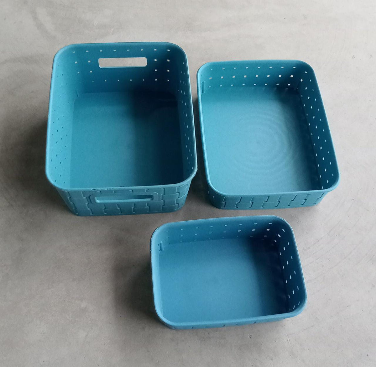 Three empty sky blue plastic storage baskets of different sizes arranged on a gray surface.