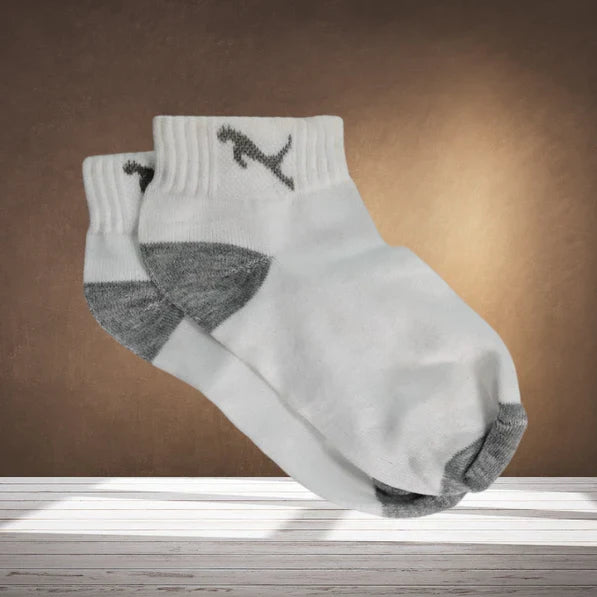 A pair of white ankle socks with grey toes and heels, and a grey puma logo, on a wooden surface.