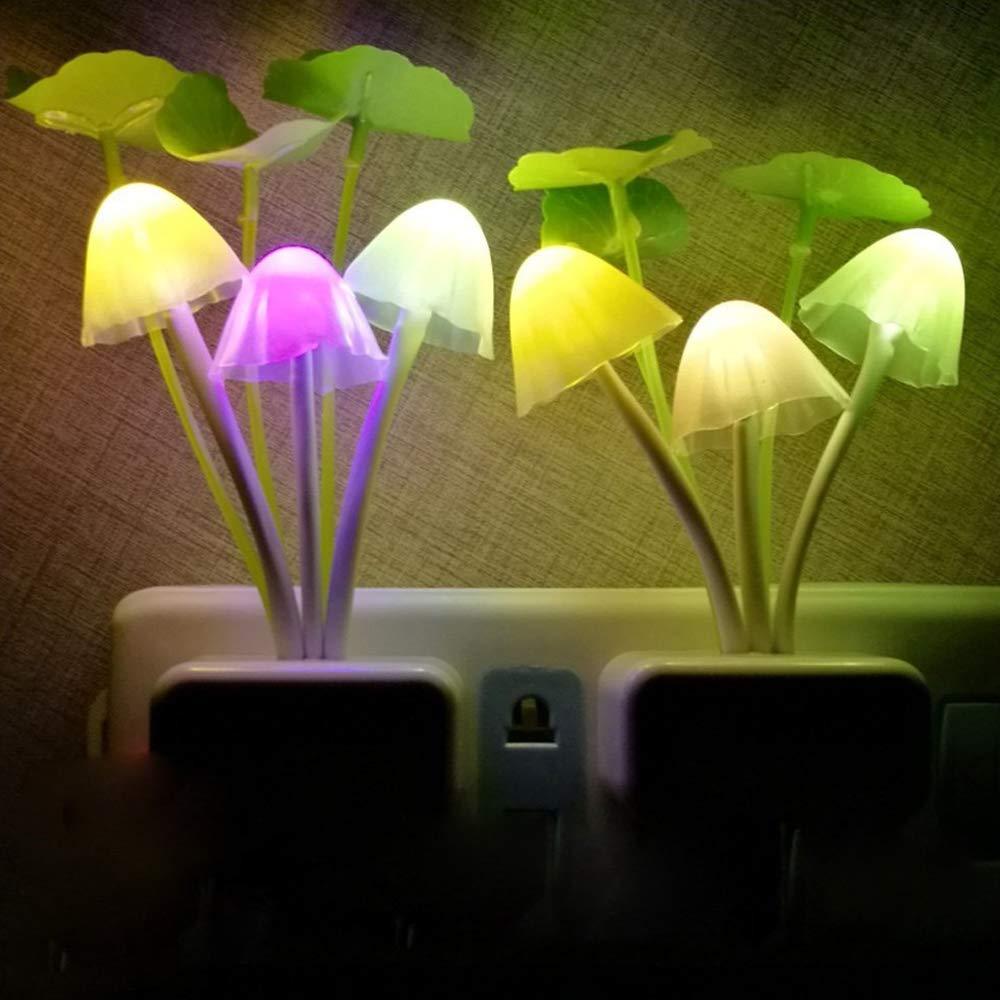 Two mushroom night lights with glowing colorful caps and green leaves are plugged into a wall outlet in a dim room.
