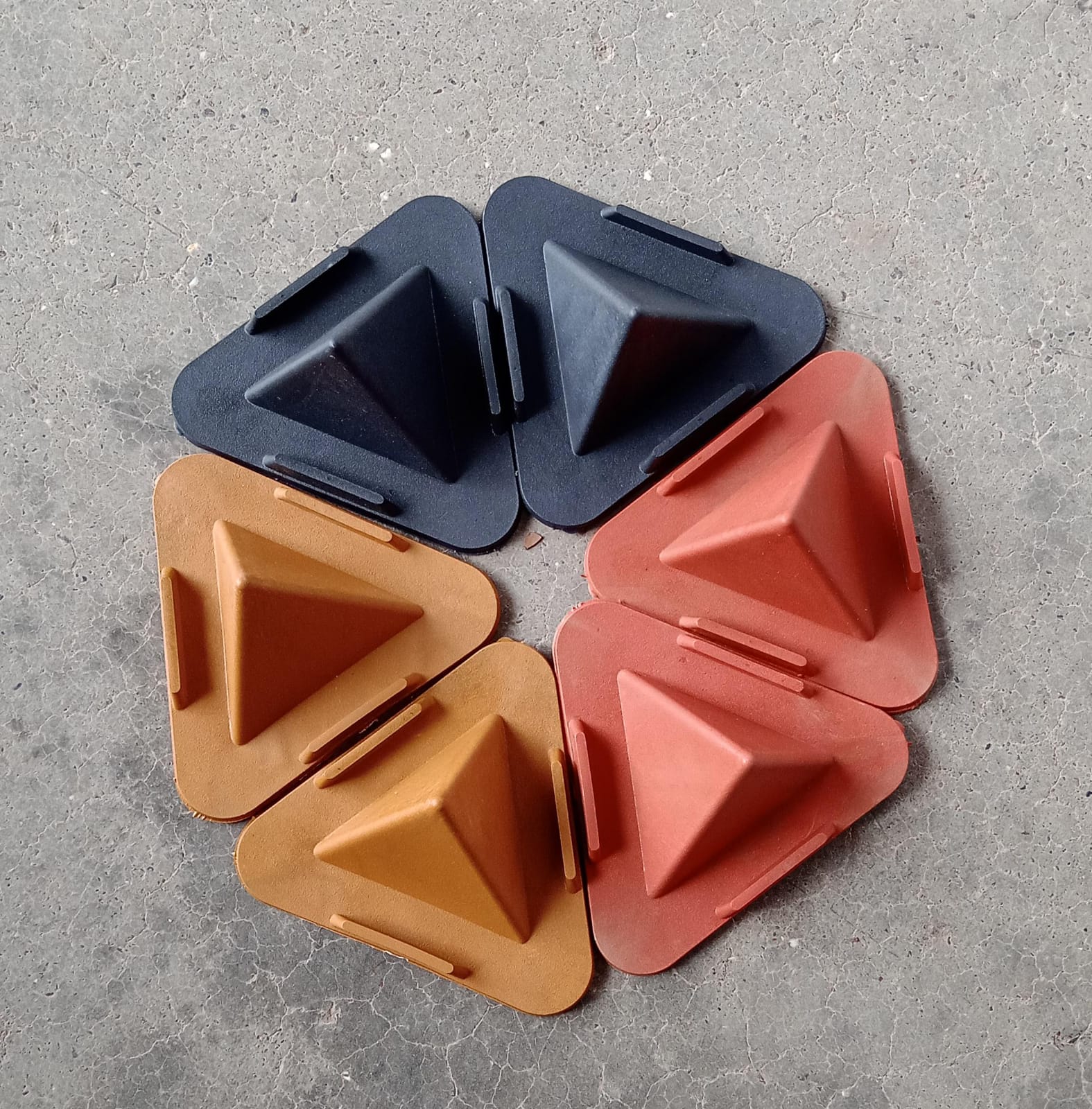 Four pyramid mobile stands in dark blue, orange, and tan are arranged in a circle on a concrete surface.