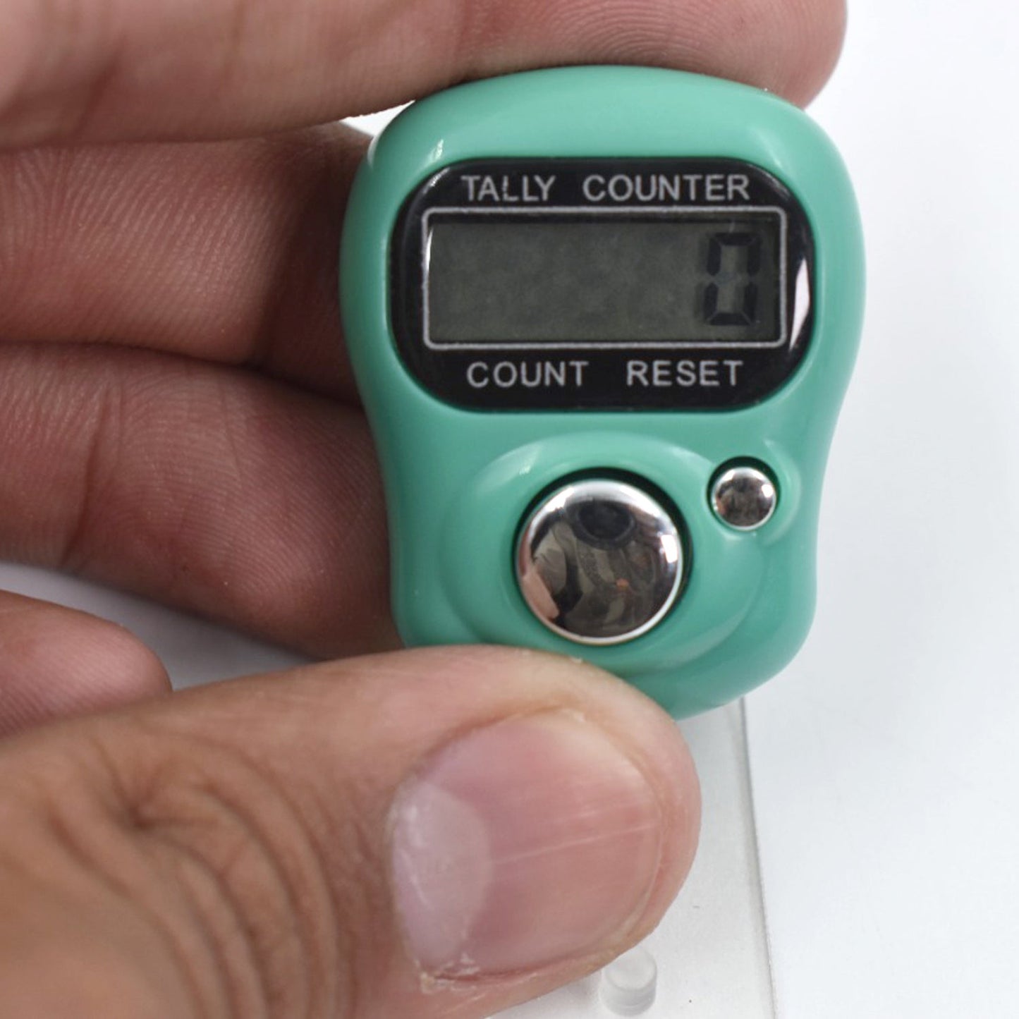 A close-up of a hand holding a green digital tally counter, showing the display with a count of 0.
