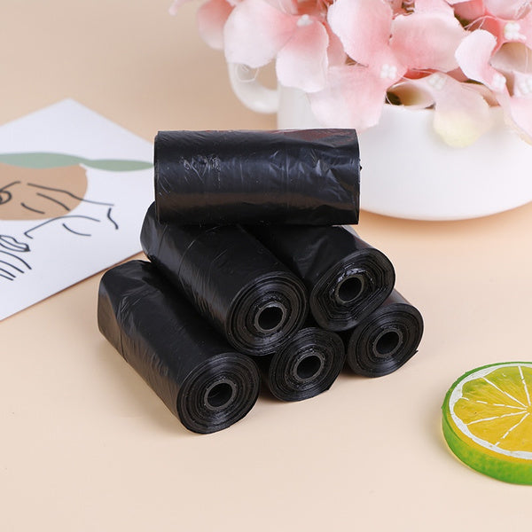 Six rolls of black garbage bags stacked on a table with a floral arrangement and decorative card.