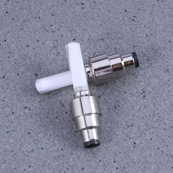 Two silver and white LED valve cap lights crossed on a speckled gray surface.