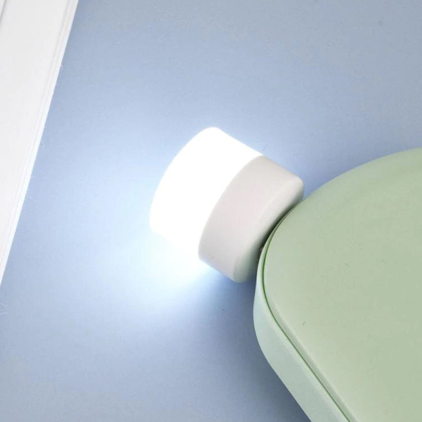 A glowing white USB LED night light is plugged into a light green power bank on a blue surface.