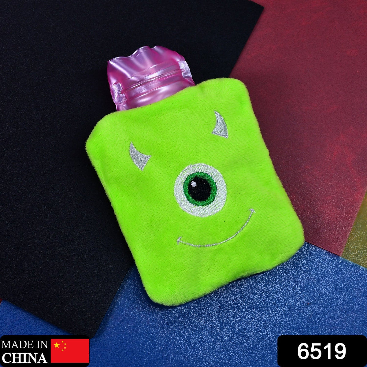 A green monster hot water bag with a pink top sits on a dark background with a "Made in China" label.