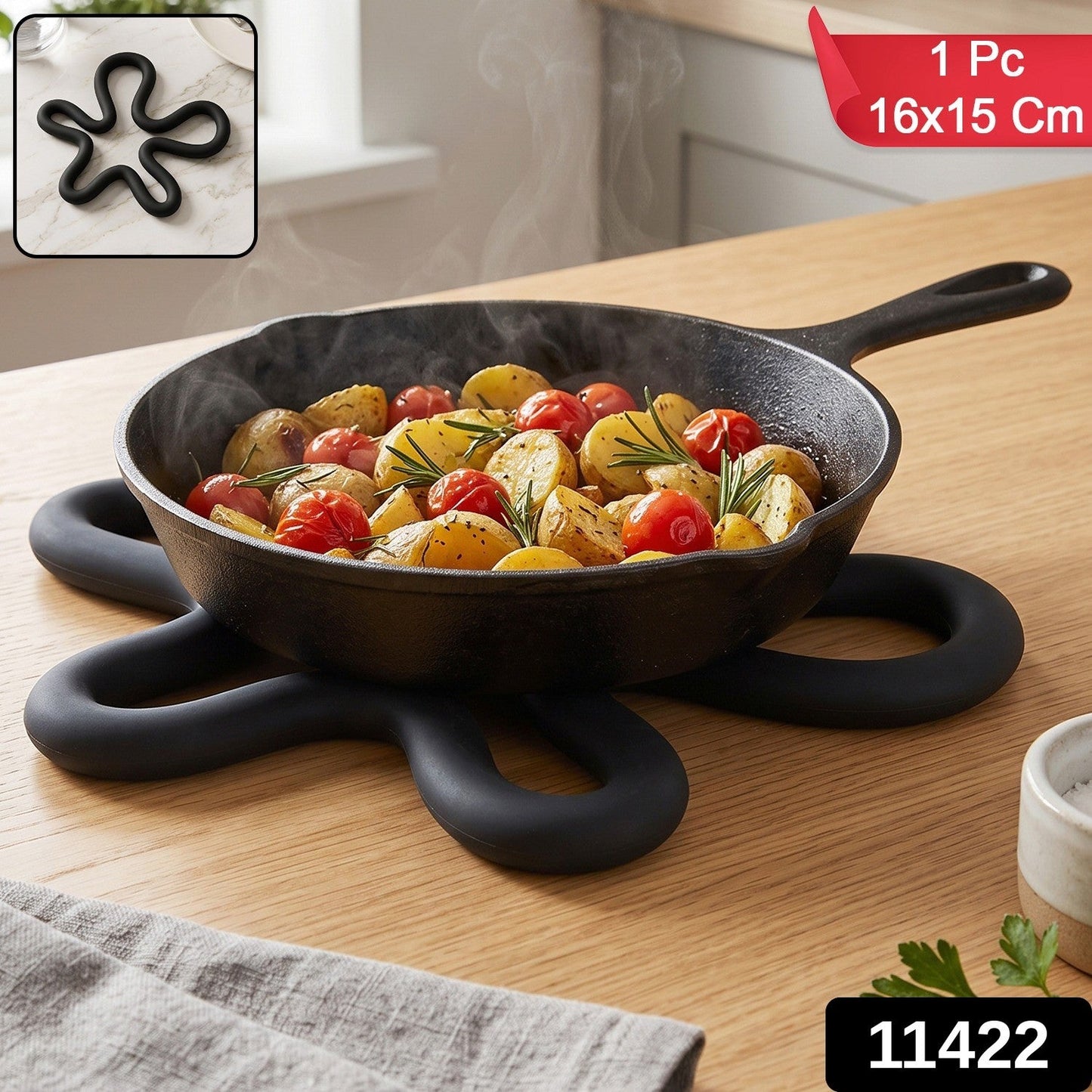 A black silicone flower-shaped hot pot holder on a wooden table, holding a cast iron pan with roasted vegetables, with