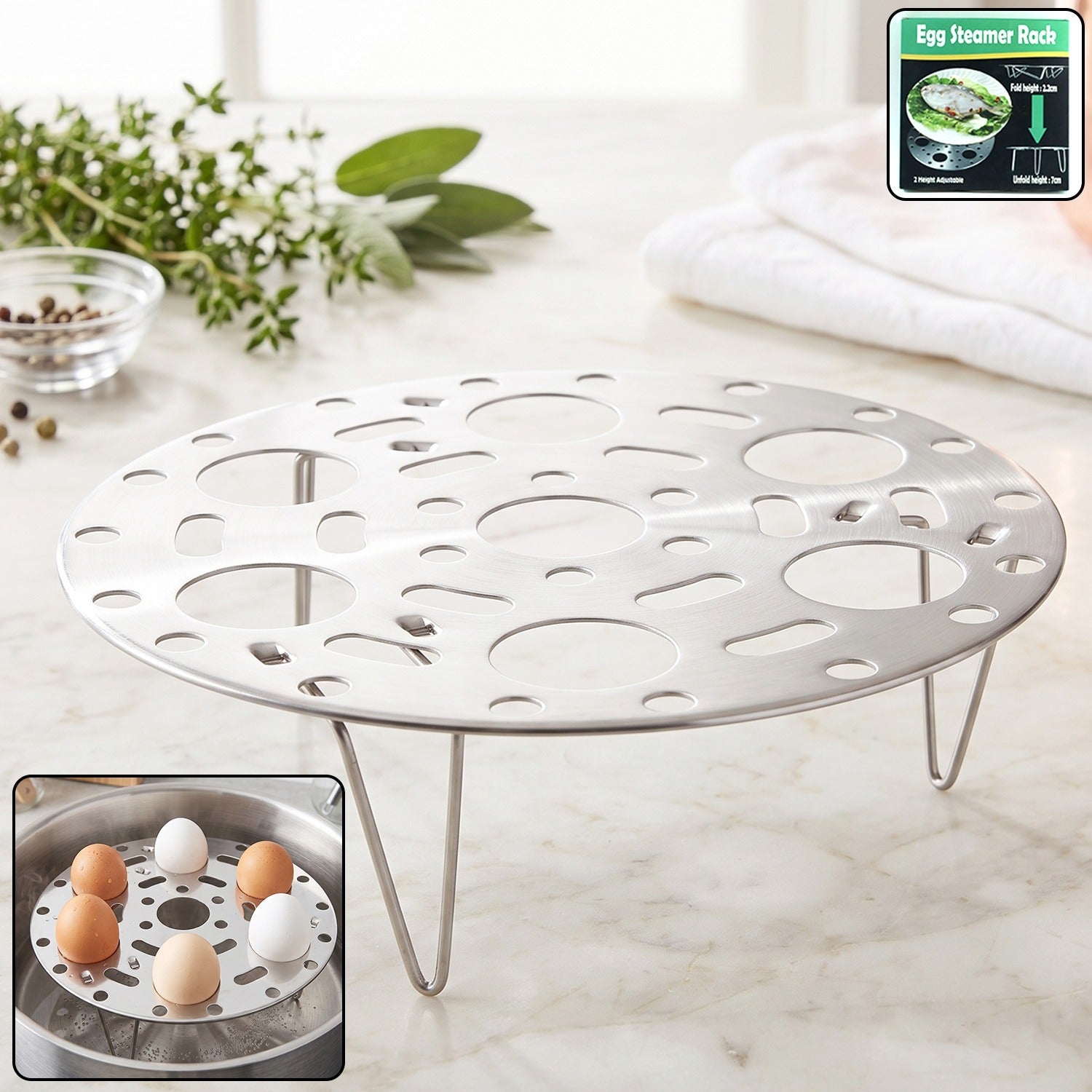 A stainless steel egg steamer rack with folding legs sits on a white marble counter, with herbs and a bowl of peppercorns in