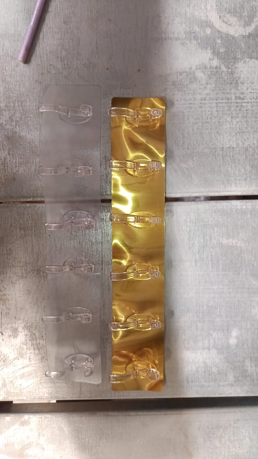 Two 6-hook adhesive wall rails, one clear and one golden, lie side-by-side on a light wooden surface.