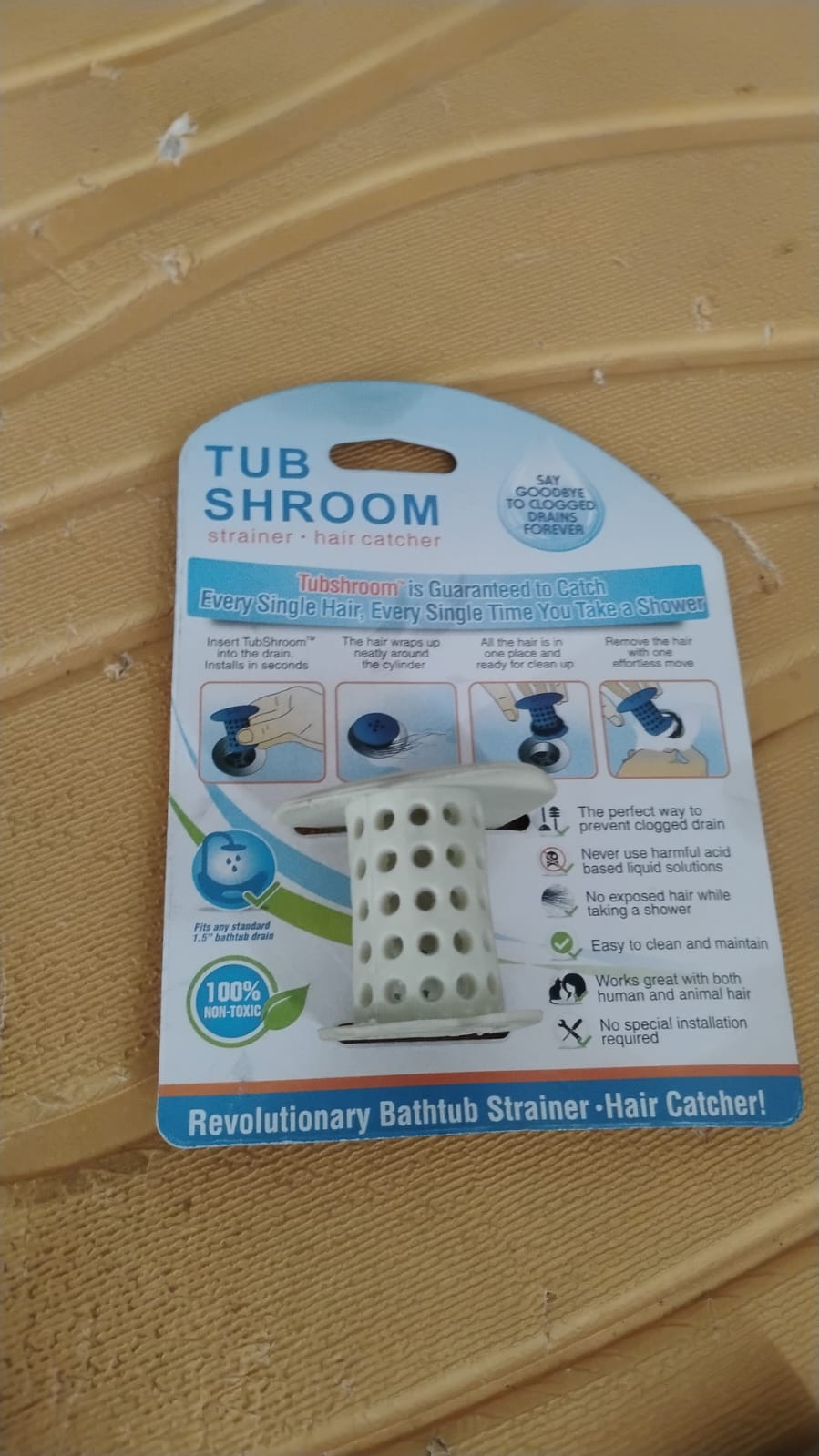 The white silicone tub drain hair catcher is shown in its retail packaging on a textured yellow surface.
