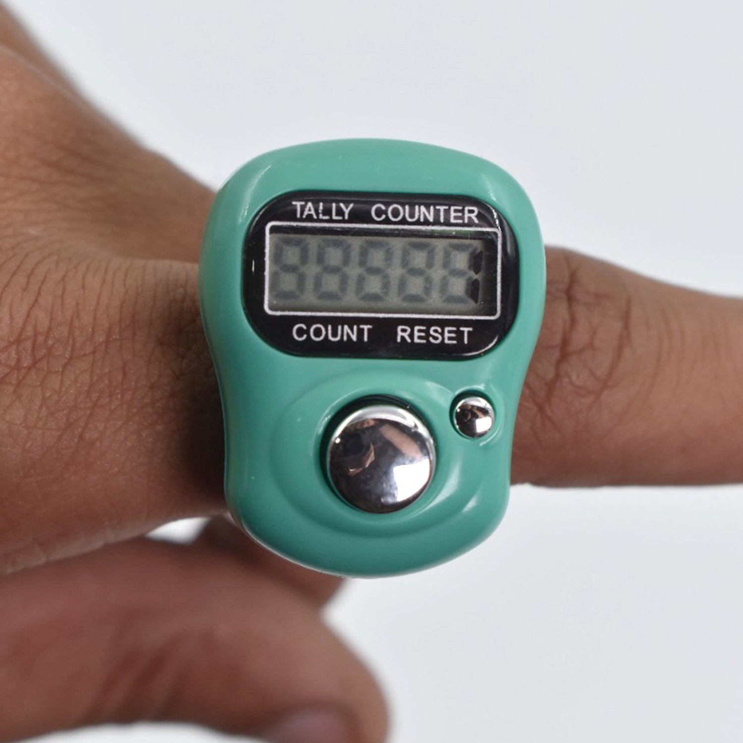 A close-up of a green digital tally counter worn on a finger, showing the display and buttons.