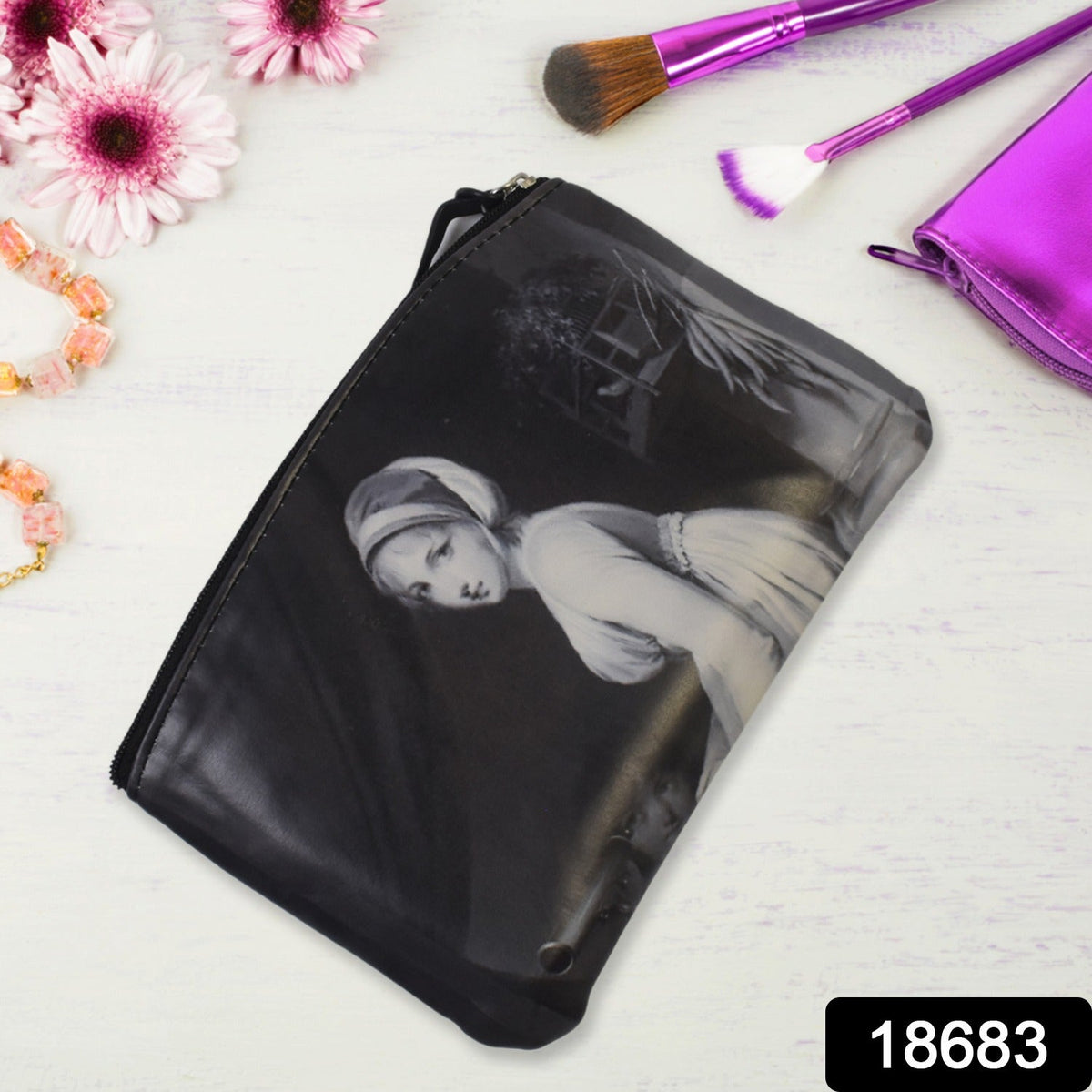 Black cosmetic bag featuring a classical portrait, resting on a white wooden surface with makeup brushes.