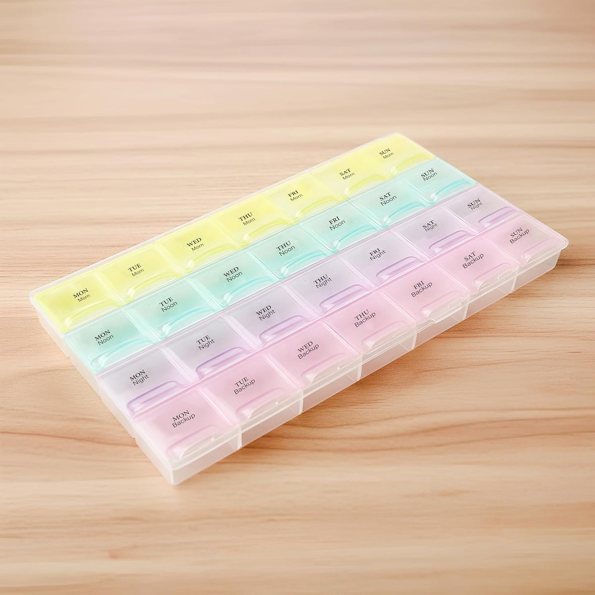 An angled view of the rainbow-colored pill organizer on a wooden surface, highlighting its translucent design.