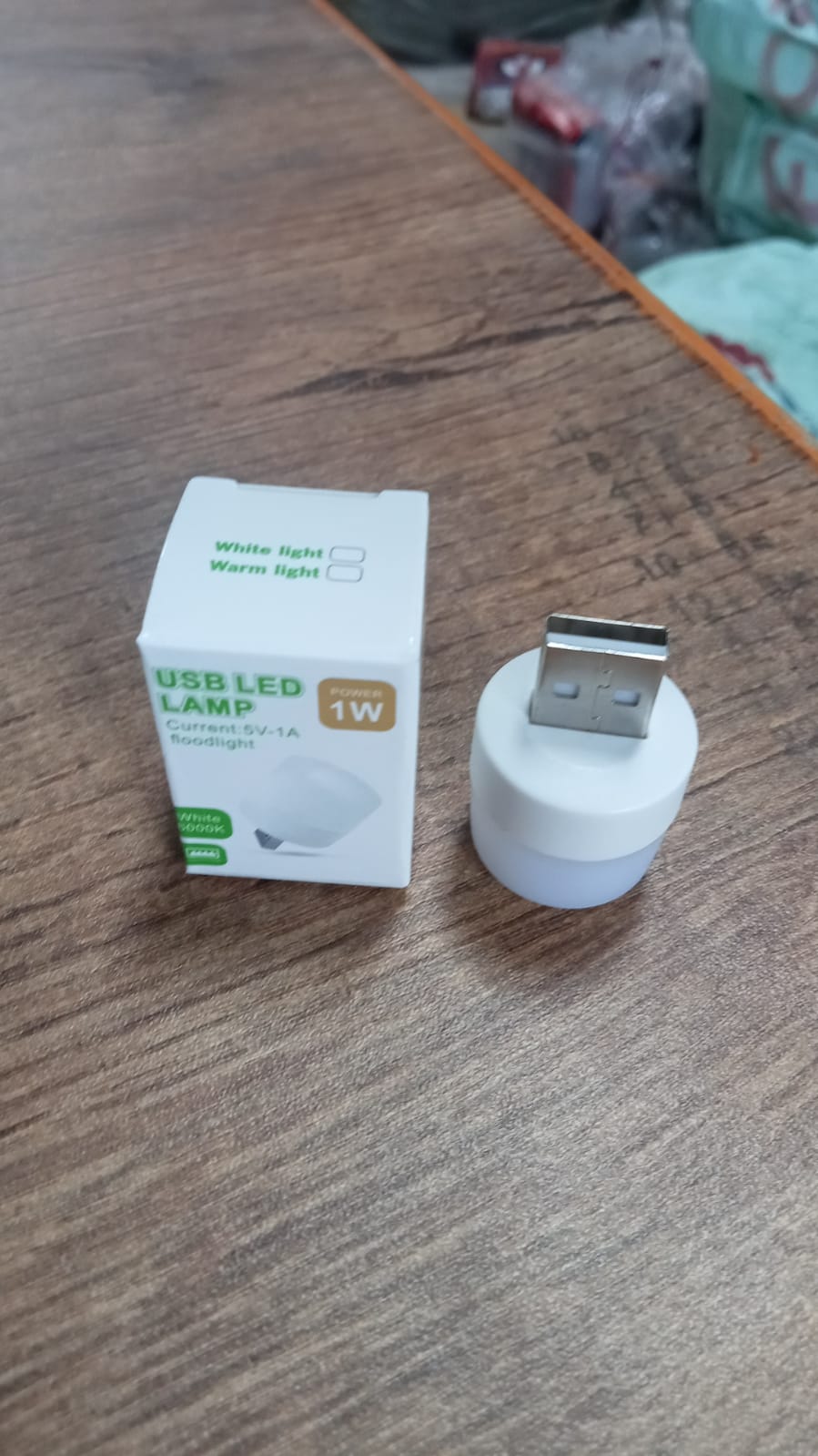 A white USB LED lamp and its packaging are placed on a wooden table, showing details of the product.