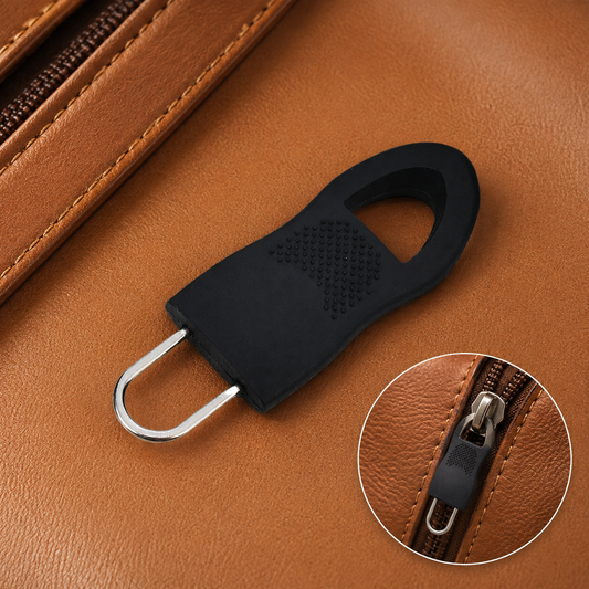 A black rubber zipper pull tab with a silver metal loop rests on a brown leather surface.