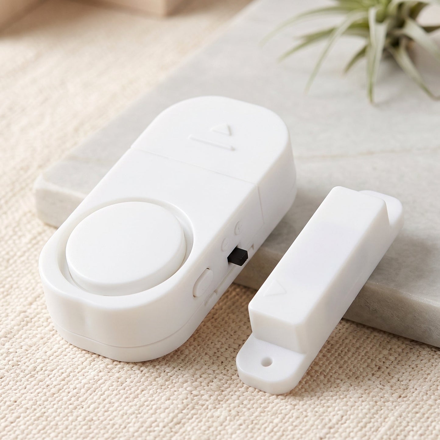 The white magnetic door alarm and its smaller magnetic component rest on a textured white surface next to a marble slab.