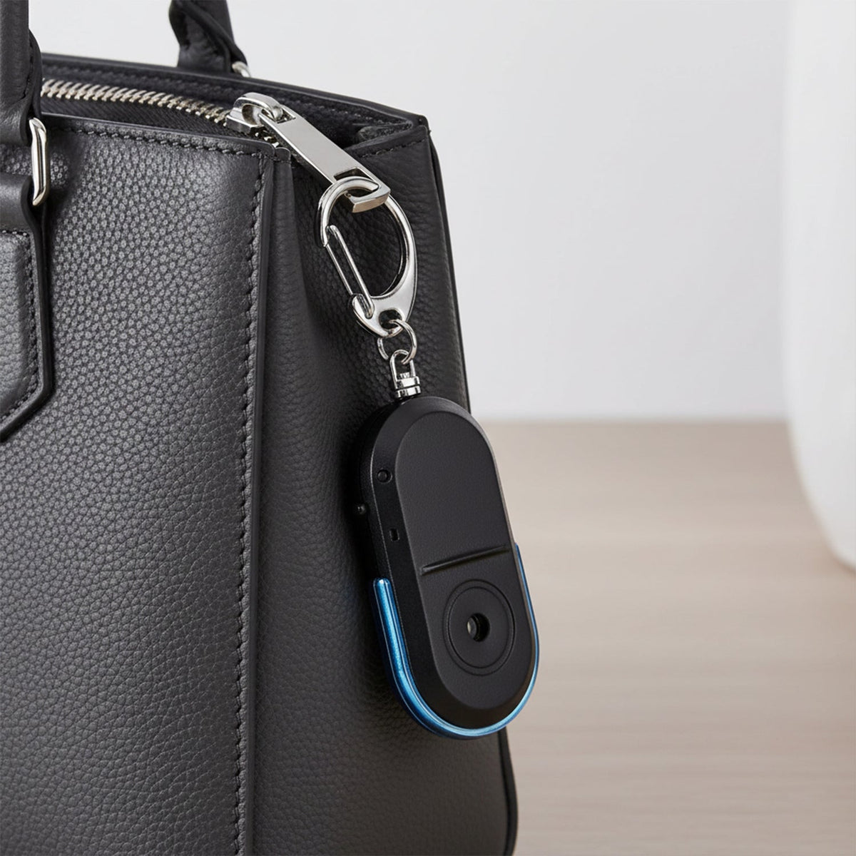 A hand holds a black and blue personal safety alarm keychain with a silver keyring.