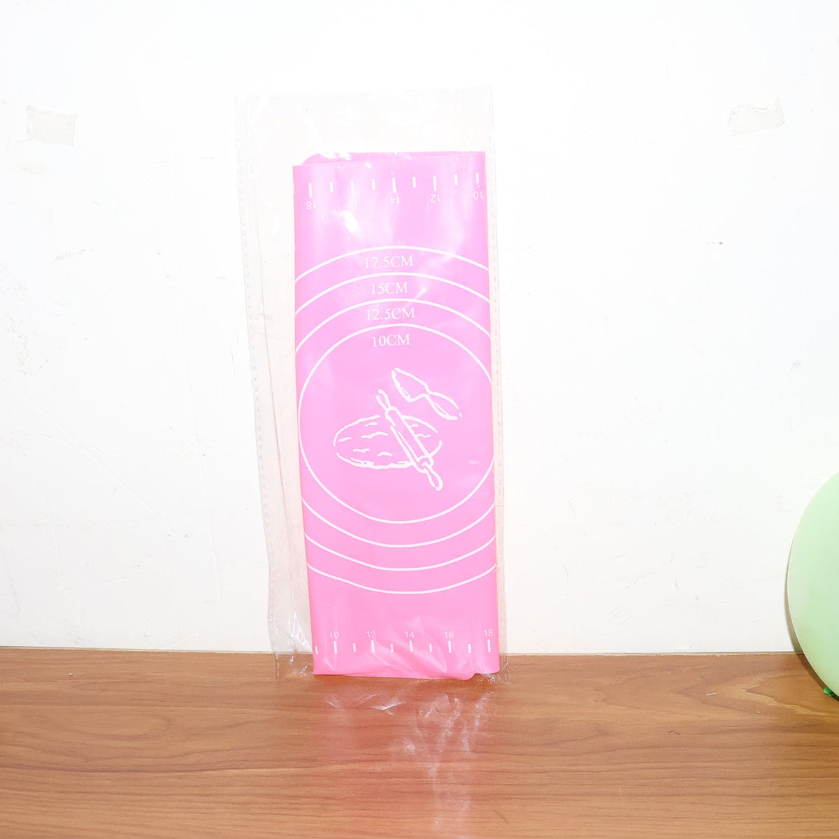 Pink silicone baking mat with white measurement guides and baking illustrations, packaged in clear plastic.