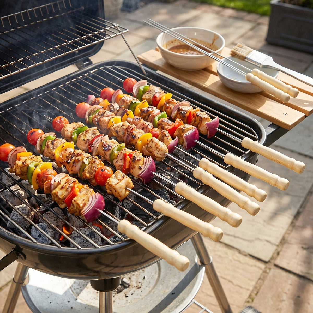 Chicken and vegetable skewers cooking on a black charcoal grill, with grilling tools on a wooden board nearby.