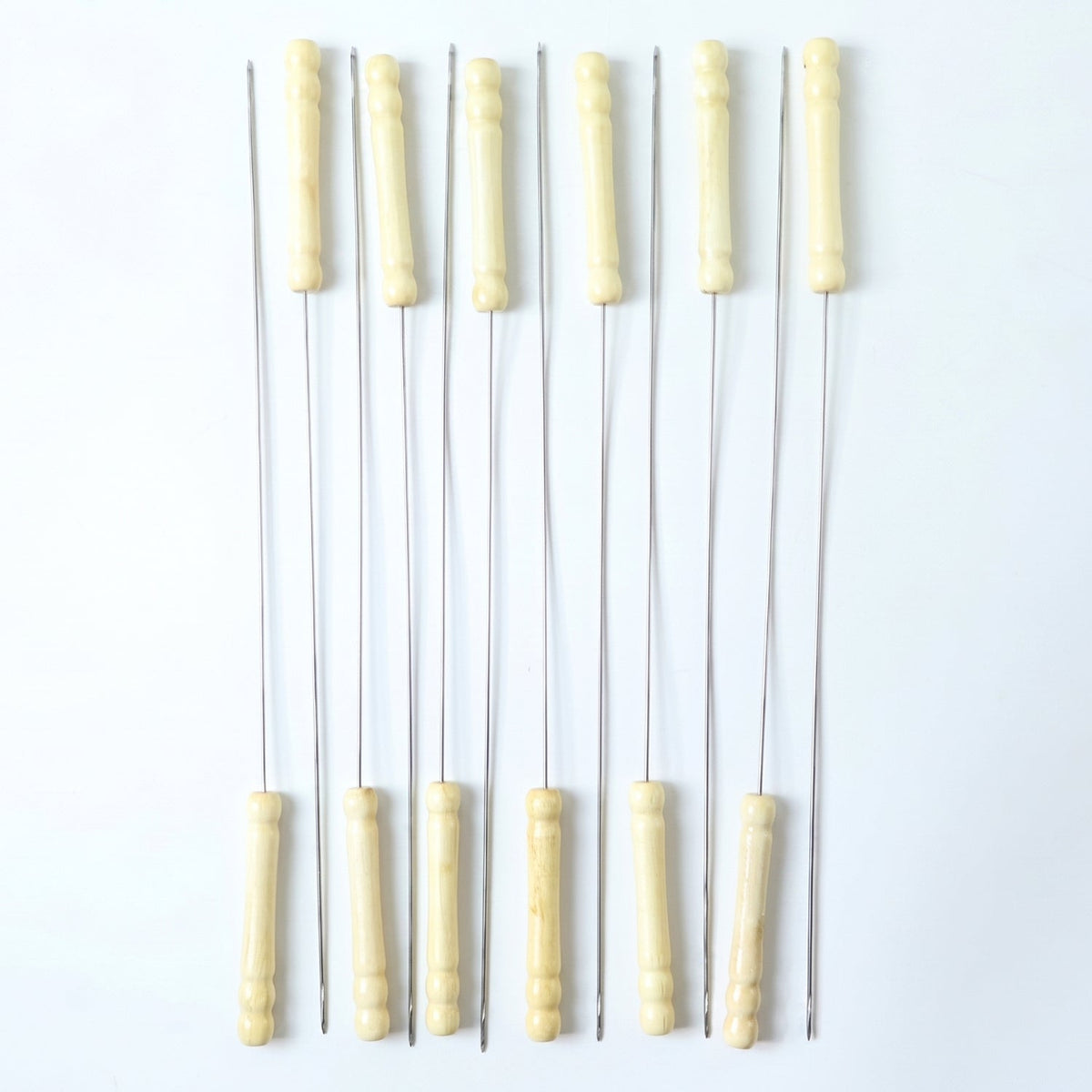 Ten stainless steel skewers with light wooden handles standing upright on a white background.