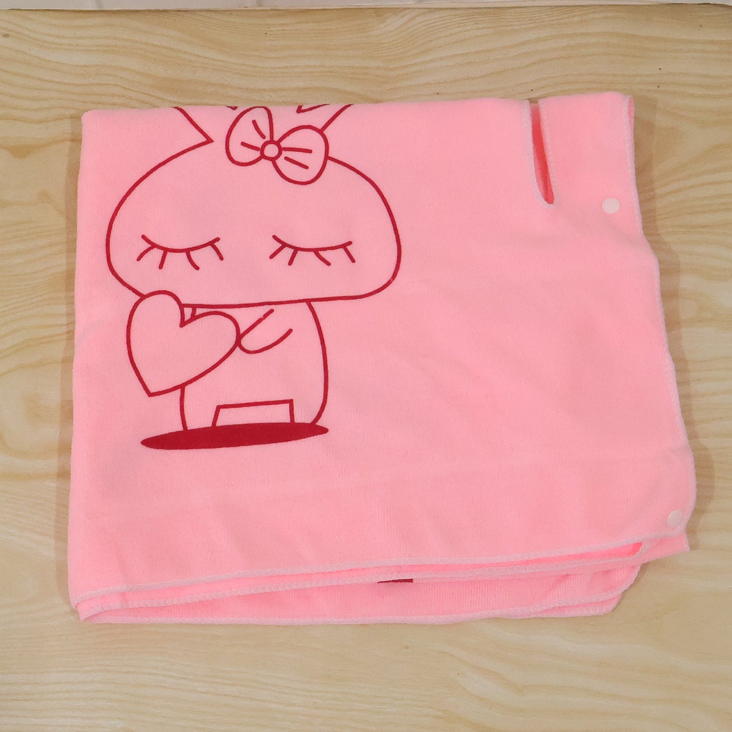 A folded pink towel with a red bunny print and white snap buttons on a wooden surface.