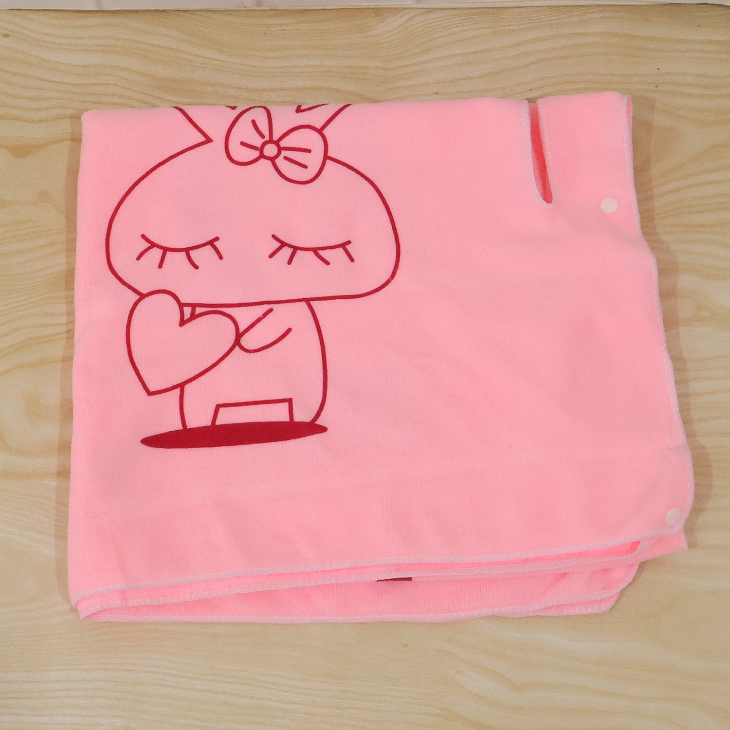 A folded pink towel with a red bunny print and white snap buttons on a wooden surface.