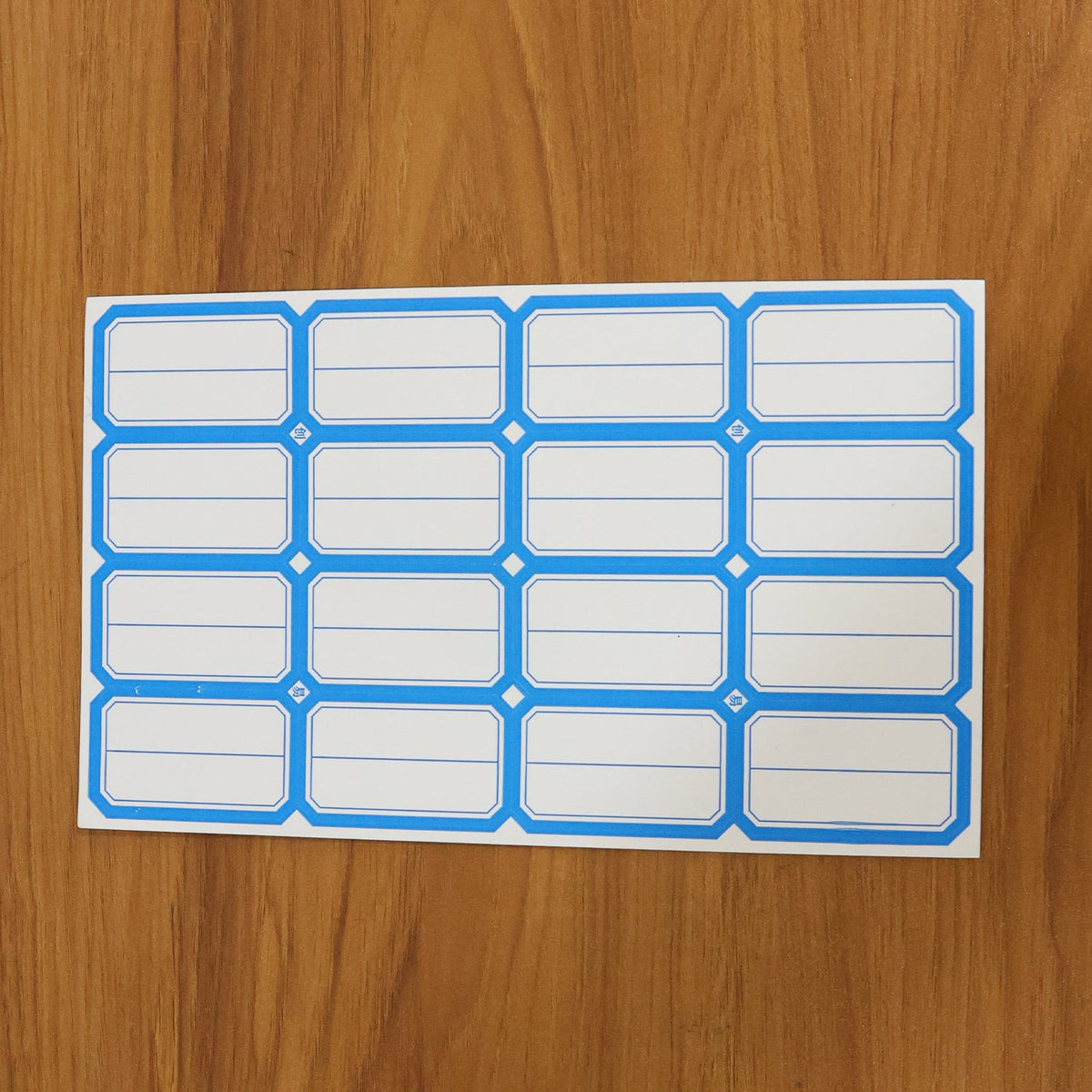 A sheet of blue-bordered rectangular label stickers with blank white centers is displayed on a wooden surface.