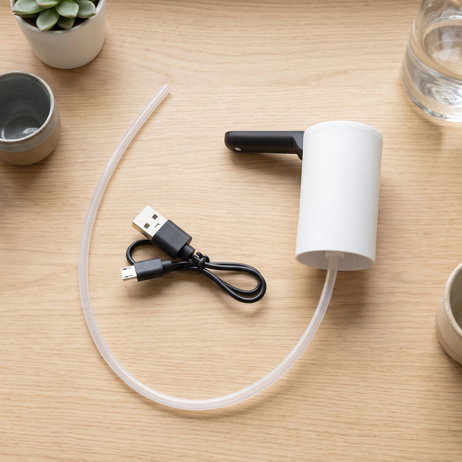 The white and black electric water dispenser pump with its clear silicone tube and black USB charging cable laid out on a