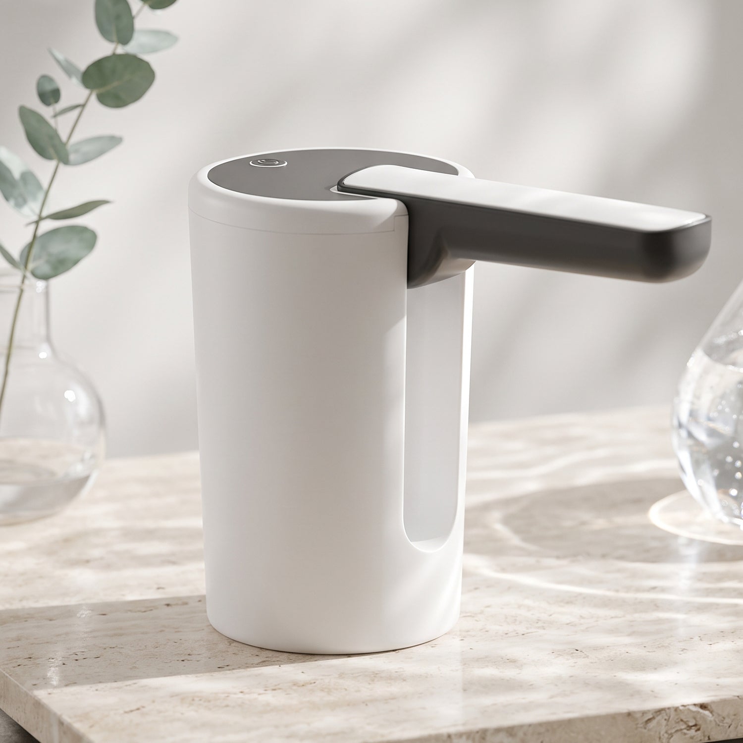 The white and black electric water dispenser pump sits on a marble surface with a glass vase holding eucalyptus branches in