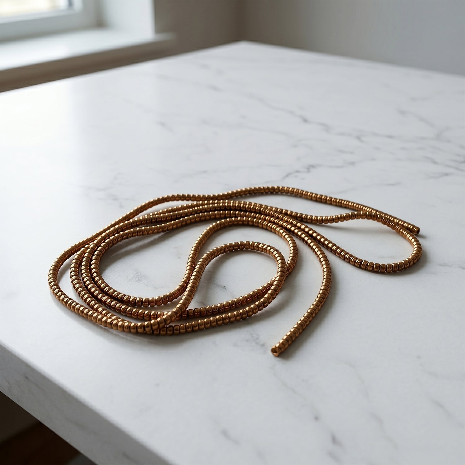 A brown spiral cable protector sleeve is loosely arranged on a white marble surface.